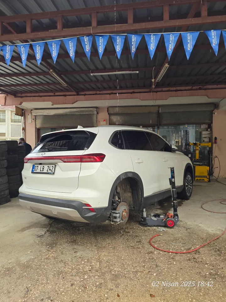 Beyaz SUV krikoyla kaldırılmış, tekerleği sökülmüş halde lastik değişimi bekliyor